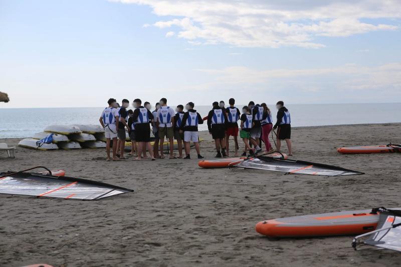 un gruppo di ragazzi ascolta l'istruttore durante una lezione di wind surf sulla spiaggia