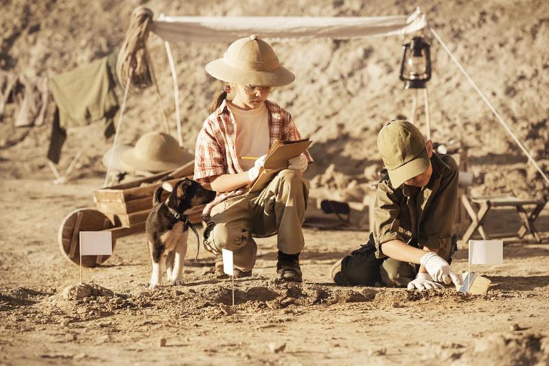Al campo archeologia due bambini con un cagnolino scavano alla ricerca di fossili