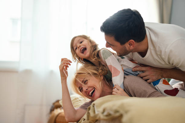 Sorridente padre e madre ridendo e giocando con la loro figlia mentre sono sdraiati su un letto.